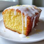 A close-up of a moist slice of lemon pound cake topped with thick white glaze and lemon zest.