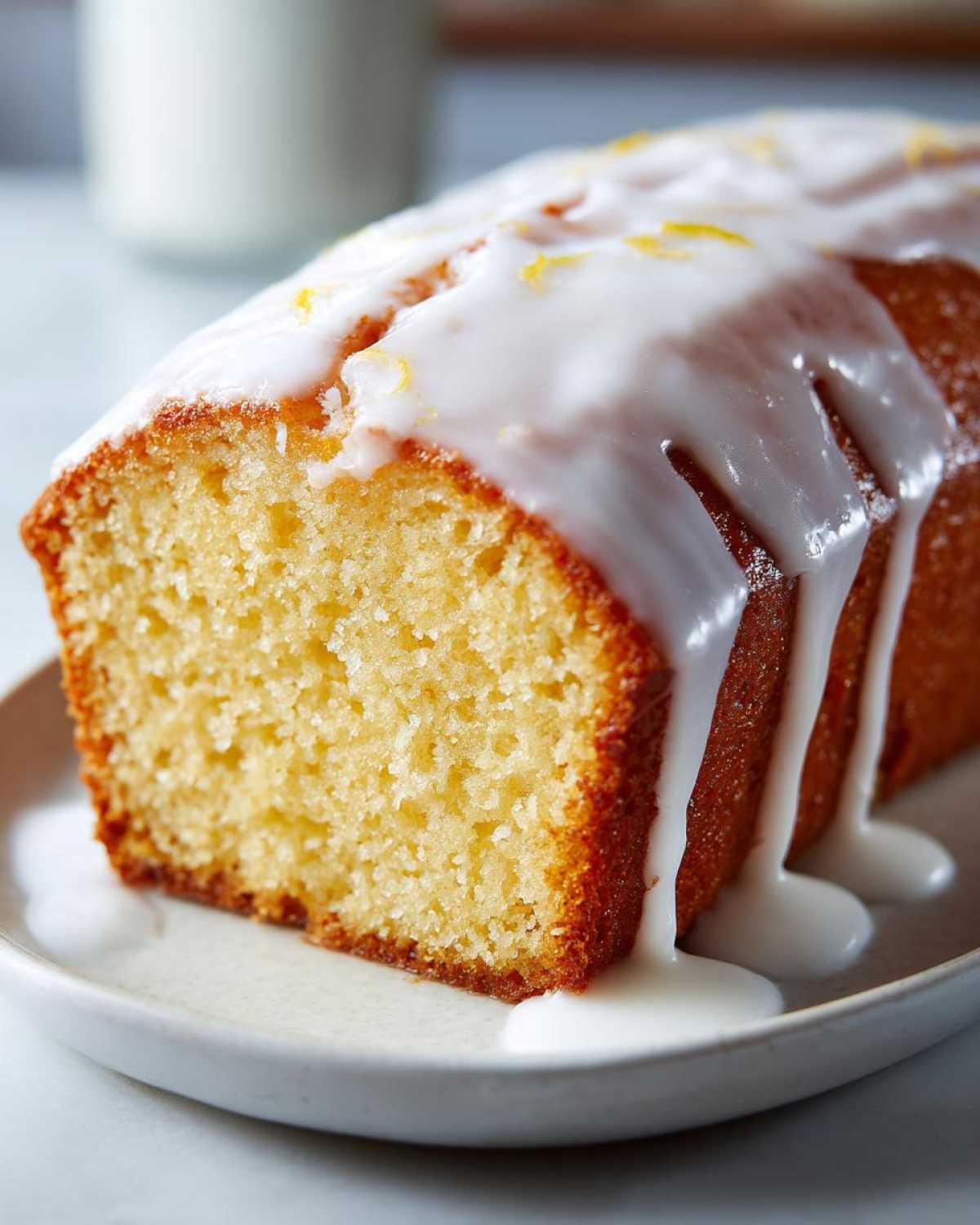 Close-up of a moist slice of lemon pound cake topped with thick white lemon glaze and zest.