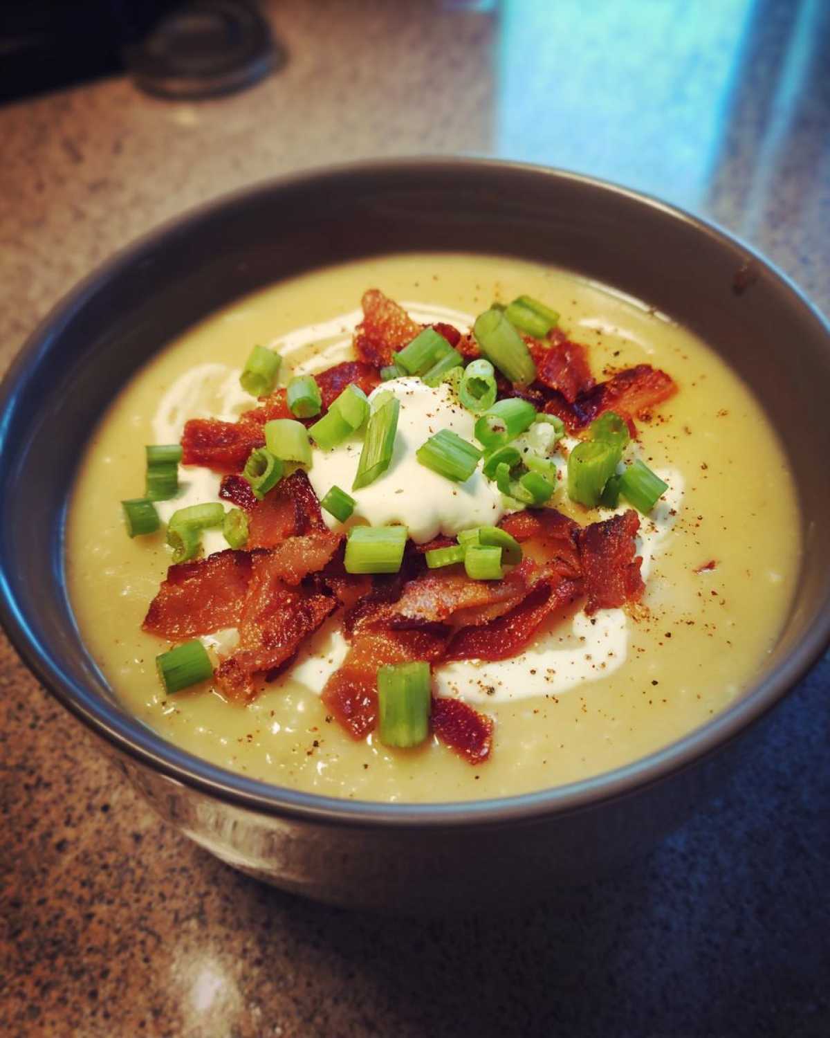 A close-up of a bowl of creamy loaded baked potato soup topped with bacon, sour cream, and green onions.