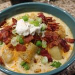 A close-up of a bowl of creamy loaded baked potato soup topped with bacon, sour cream, and green onions.