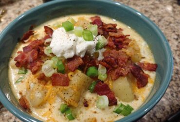 A close-up of a bowl of creamy loaded baked potato soup topped with bacon, sour cream, and green onions.