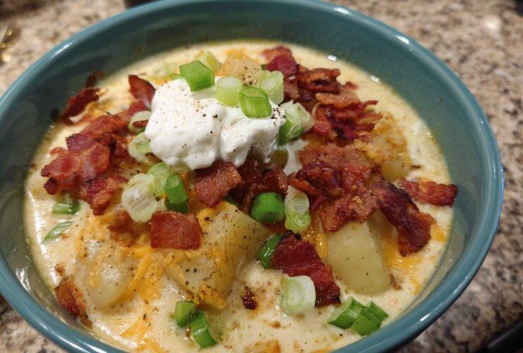 A close-up of a bowl of creamy loaded baked potato soup topped with bacon, sour cream, and green onions.