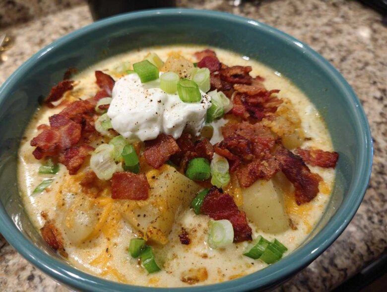 A close-up of a bowl of creamy loaded baked potato soup topped with bacon, sour cream, and green onions.