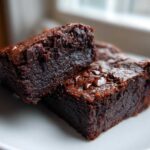 Two rich, fudgy pieces of black bean brownies stacked slightly on a white plate, showing melted chocolate chips.