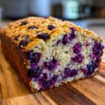 Close-up of a freshly baked blueberry banana bread loaf showing moist crumb and bursting blueberries.