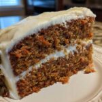 Close-up of a thick, moist slice of carrot cake recipe layered with cream cheese frosting and pecans.