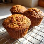 Close-up of three golden brown honey bran muffins cooling on a wire rack in natural light.