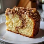 Close-up of a moist slice of sour cream coffee cake featuring a rich cinnamon swirl and thick crumbly streusel topping.