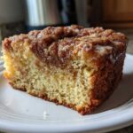 A close-up of a moist slice of sour cream coffee cake featuring a cinnamon swirl and light glaze.