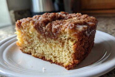A close-up of a moist slice of sour cream coffee cake featuring a cinnamon swirl and light glaze.