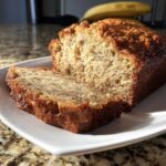A close-up of a thick slice of moist sugar free banana bread on a white plate.