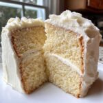 Close-up of a slice cut from a moist vanilla cake recipe, showing fluffy layers and white frosting.