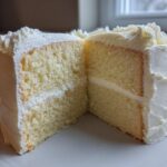 Cross-section of a moist vanilla cake recipe slice showing two layers and white frosting.