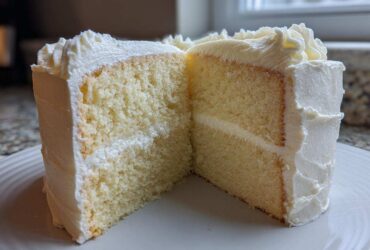 Cross-section of a moist vanilla cake recipe slice showing two layers and white frosting.