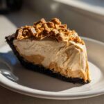 A rich slice of no-bake peanut butter pie with a dark crust, creamy filling, and crunchy topping.