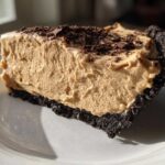 Close-up of a thick slice of no-bake peanut butter pie featuring a creamy filling and dark chocolate crust, topped with chocolate shavings.