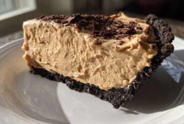 Close-up of a thick slice of no-bake peanut butter pie featuring a creamy filling and dark chocolate crust, topped with chocolate shavings.