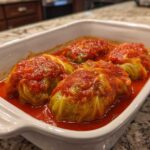 Four delicious cabbage rolls simmering in a vibrant red tomato sauce inside a white baking dish.
