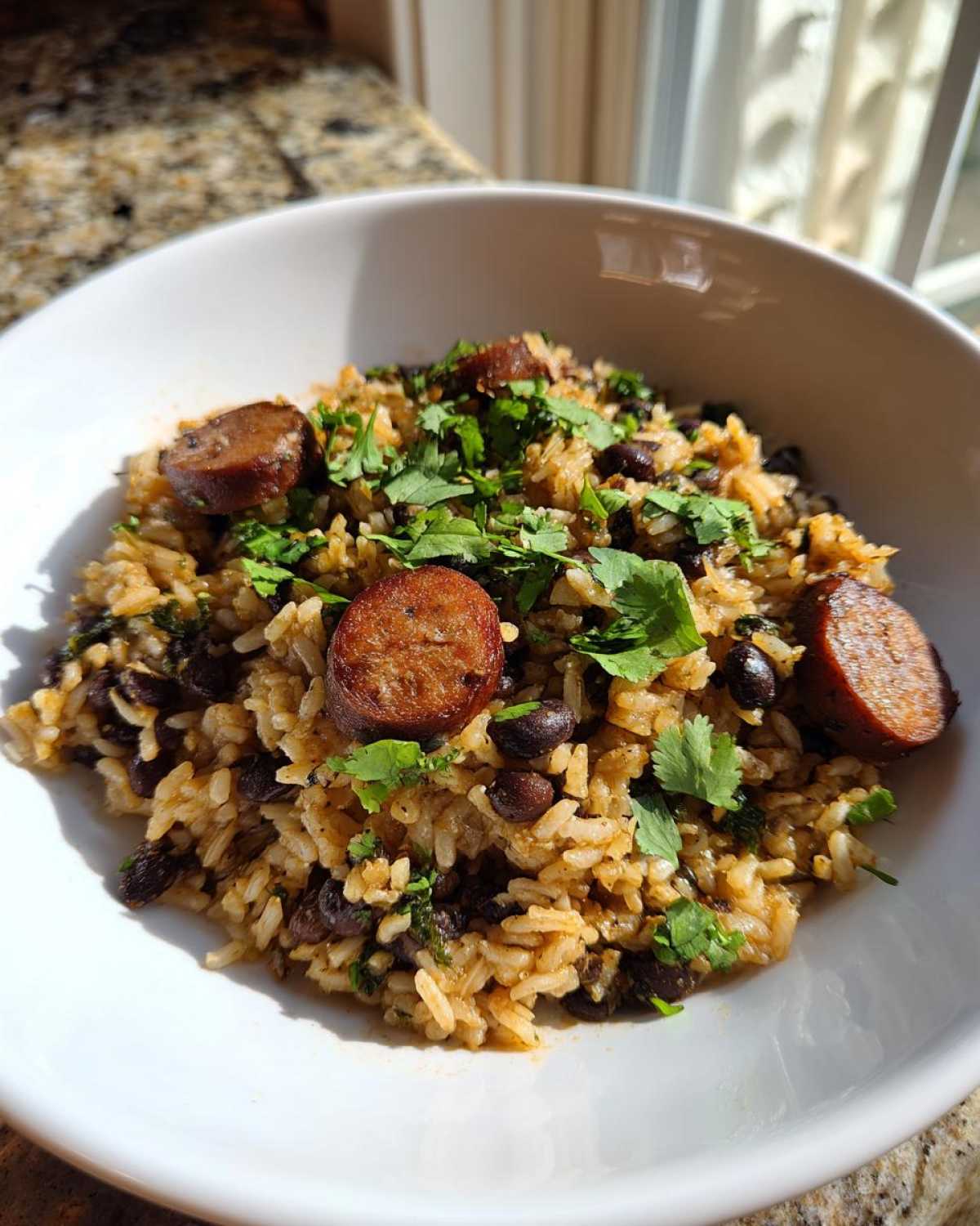 A close-up serving of flavorful 1-pot black beans and rice mixed with dark beans and topped with sliced sausage and fresh cilantro.