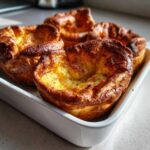 Four golden brown, perfectly risen yorkshire pudding baked in a white ceramic dish.