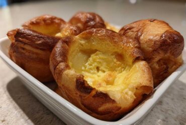 A close-up of several golden brown, perfectly risen Yorkshire pudding baked in a white rectangular dish.
