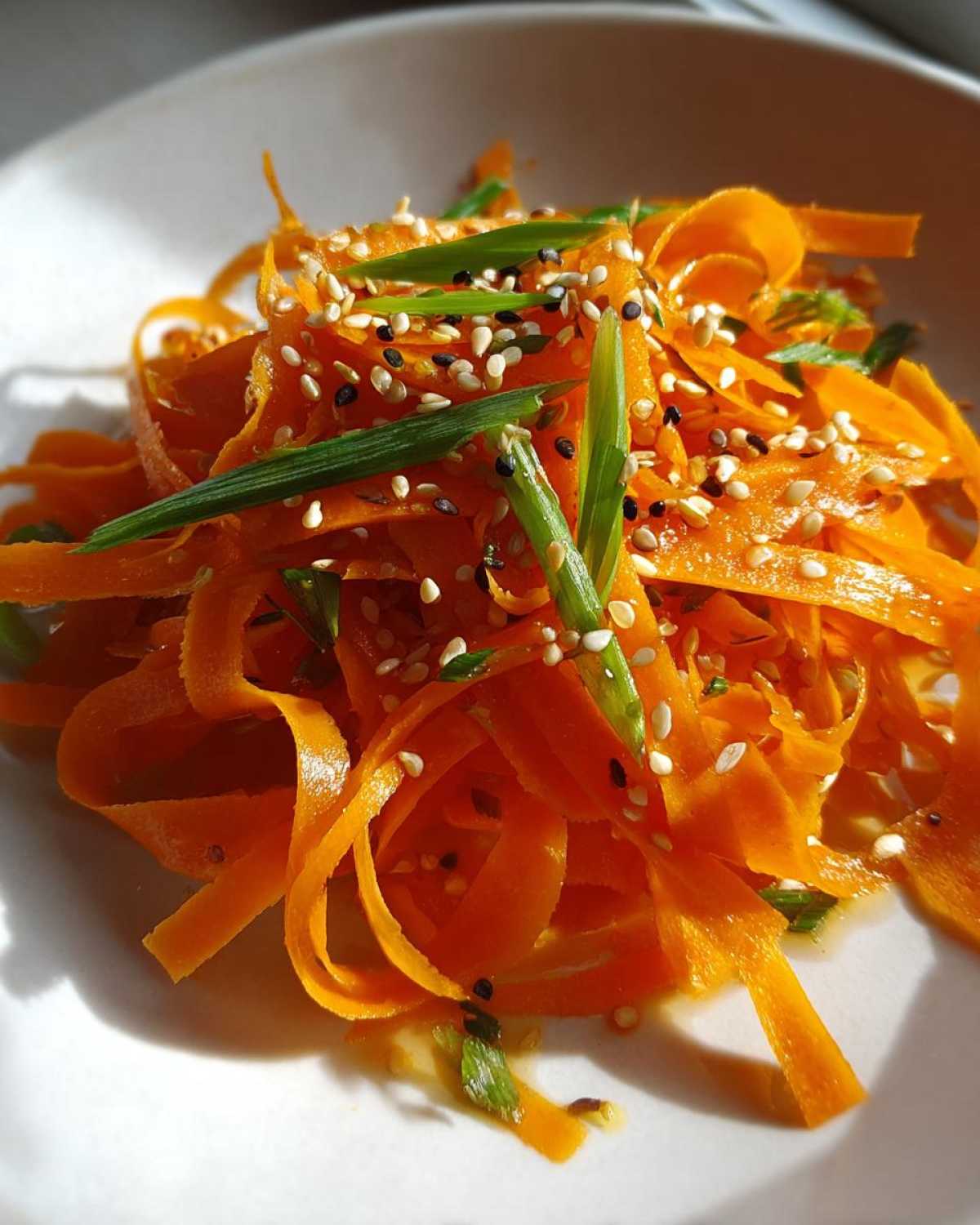 Close-up of a vibrant raw carrot salad made with shaved carrots, topped with sesame seeds and green onions.