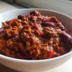 Close-up of a hearty bowl of rich, saucy crockpot chili filled with ground meat and kidney beans.