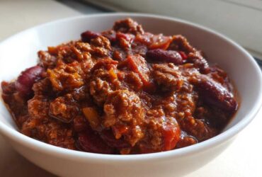 Close-up of a hearty bowl of rich, saucy crockpot chili filled with ground meat and kidney beans.