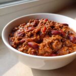 Close-up of a white bowl filled with rich, thick crockpot chili featuring ground meat and red kidney beans.
