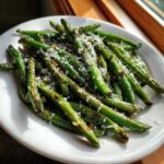 A close-up of bright, roasted green beans topped with grated Parmesan cheese on a white plate.