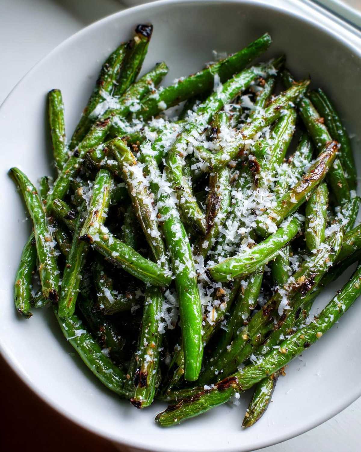 Close-up of roasted green beans topped with grated Parmesan cheese in a white bowl.