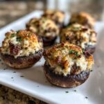 Two golden-brown Sausage stuffed mushrooms in the foreground, garnished with parsley, served on a white platter.