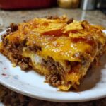 A close-up serving of Dorito Casserole featuring layers of seasoned ground beef, creamy sauce, and melted cheddar cheese topped with chips.