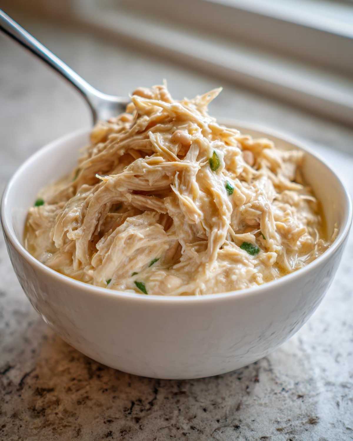 Close-up of shredded chicken and beans in a creamy sauce, ready for crockpot white chicken chili.