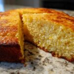 Close-up of a golden brown skillet cornbread with one wedge cut out, showing the moist, crumbly texture inside.