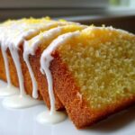 Close-up of a sliced lemon pound cake topped with thick white glaze dripping down the sides and sprinkled with zest.