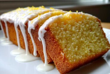 Close-up of a sliced lemon pound cake topped with thick white glaze dripping down the sides and sprinkled with zest.