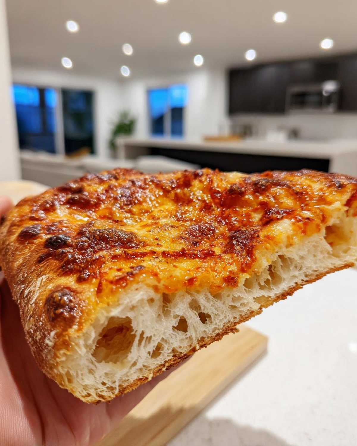 Close-up of a thick slice of pizza made with sourdough discard pizza dough, showing a light, airy crumb and bubbly, browned cheese topping.