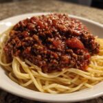 A close-up of spaghetti topped generously with rich, meaty bolognese sauce and a sprinkle of parmesan cheese.