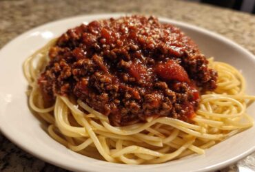 A close-up of spaghetti topped generously with rich, meaty bolognese sauce and a sprinkle of parmesan cheese.