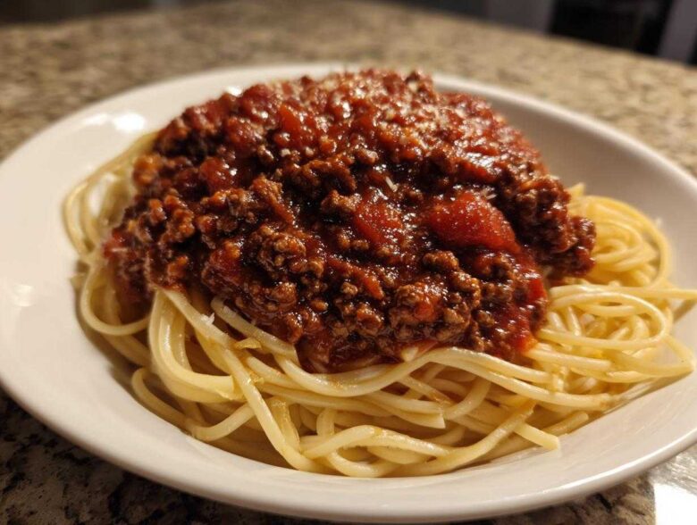 A close-up of spaghetti topped generously with rich, meaty bolognese sauce and a sprinkle of parmesan cheese.