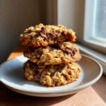 A stack of three homemade oatmeal cookie with visible chocolate chunks, sitting on a small plate.