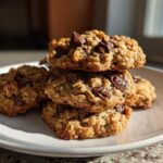 A stack of four golden brown, chewy oatmeal cookie loaded with melted chocolate chips, sitting on a white plate.