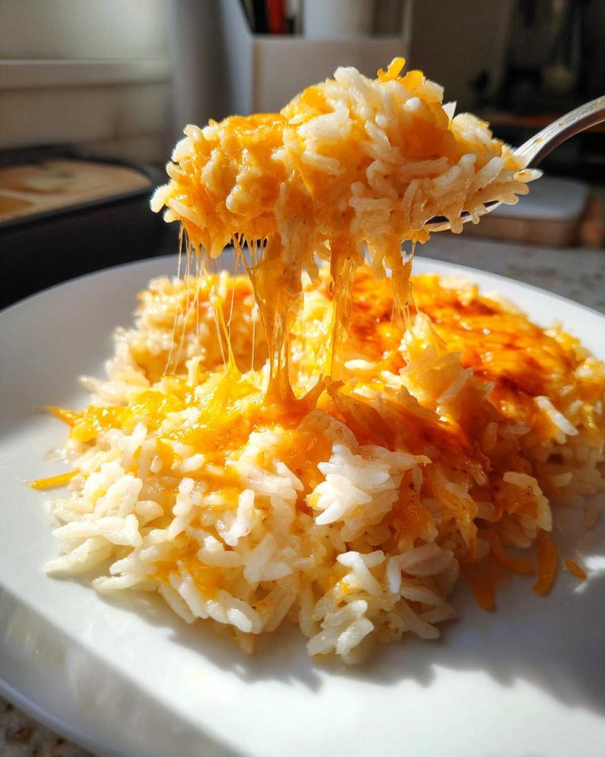 A spoonful of cheesy rice lifted, showing long, melted cheese strings stretching from the main serving on the plate.