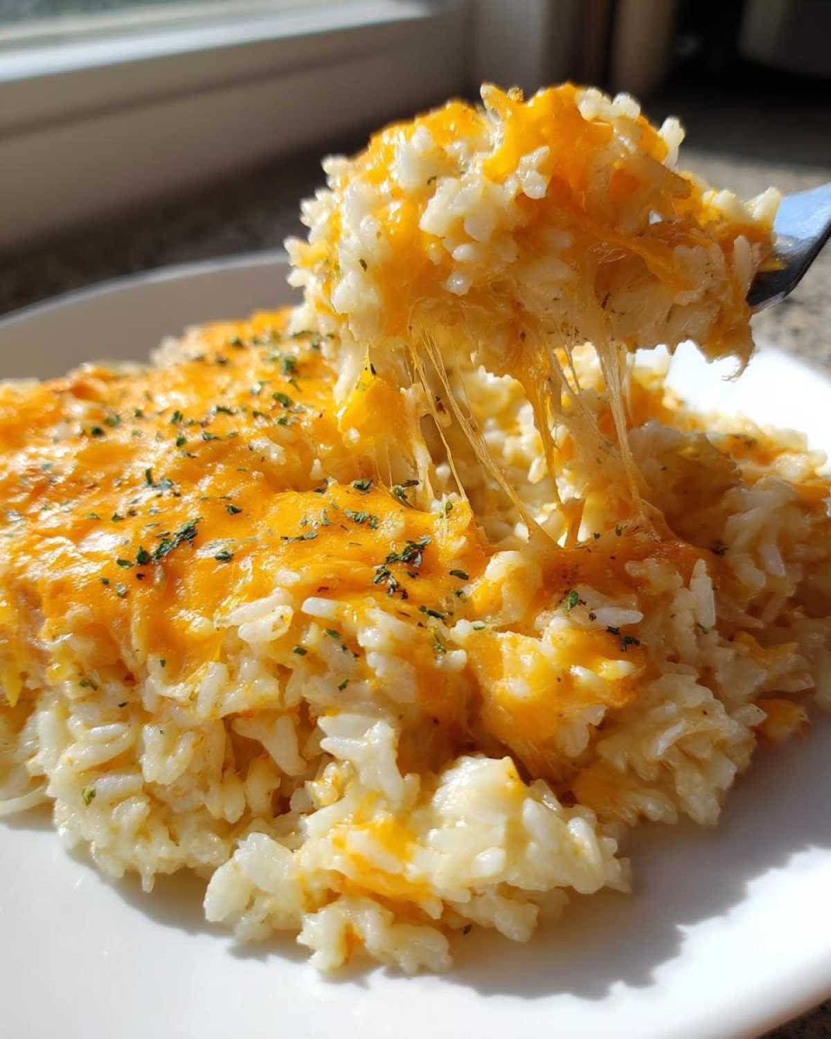 A fork lifts a bite of creamy, cheesy rice, showing long, melted cheese strands in this amazing cheesy rice dish.