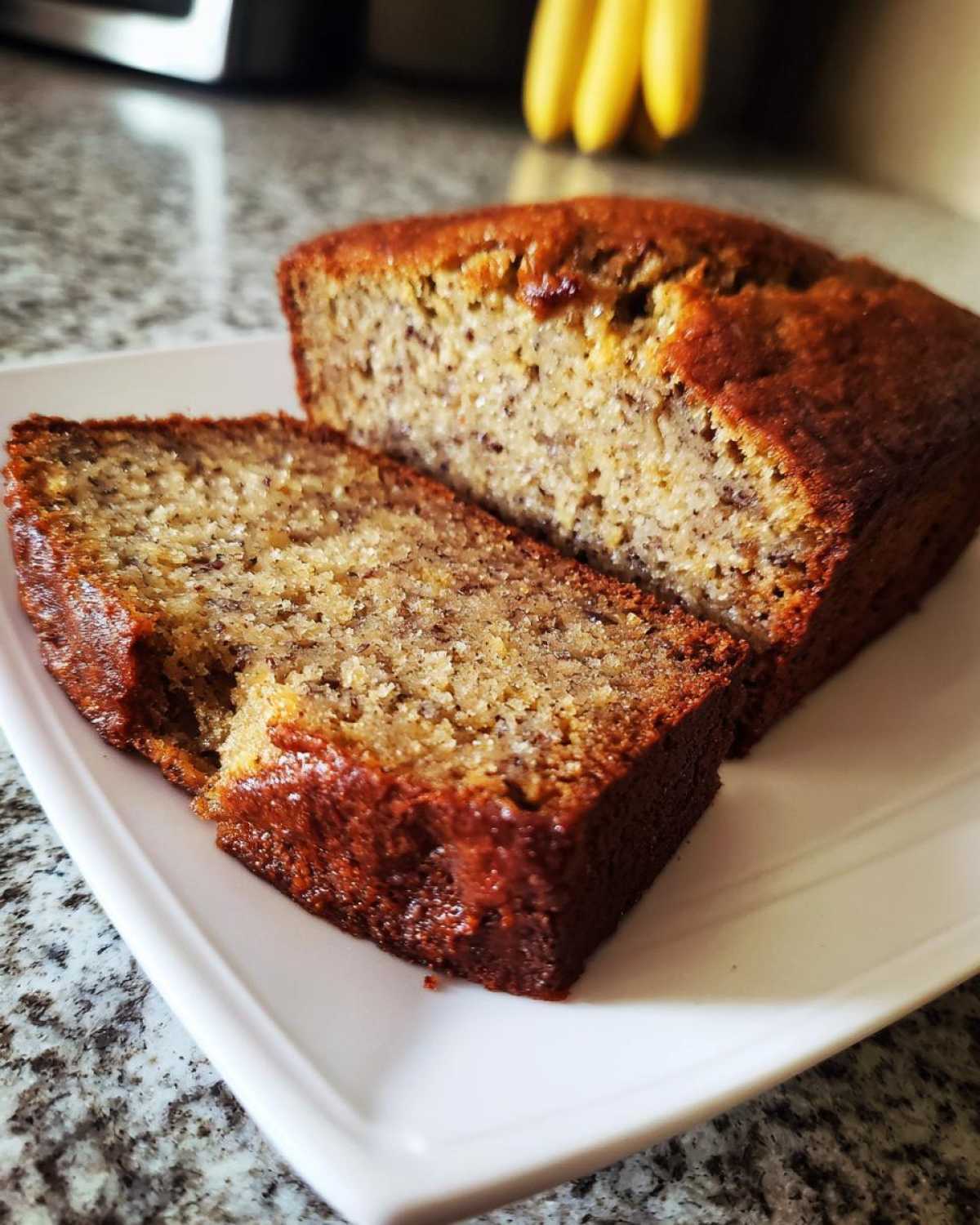 Close-up of a moist slice of sugar free banana bread next to the rest of the loaf on a white plate.
