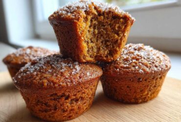 A stack of moist, brown bran muffins topped with coarse sugar crystals, one muffin is broken open.