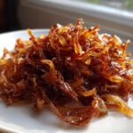 A close-up of a mound of deeply browned, glossy caramelized onions on a white plate.