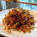 A close-up shot of a mound of deeply browned, sweet caramelized onions resting on a white plate.