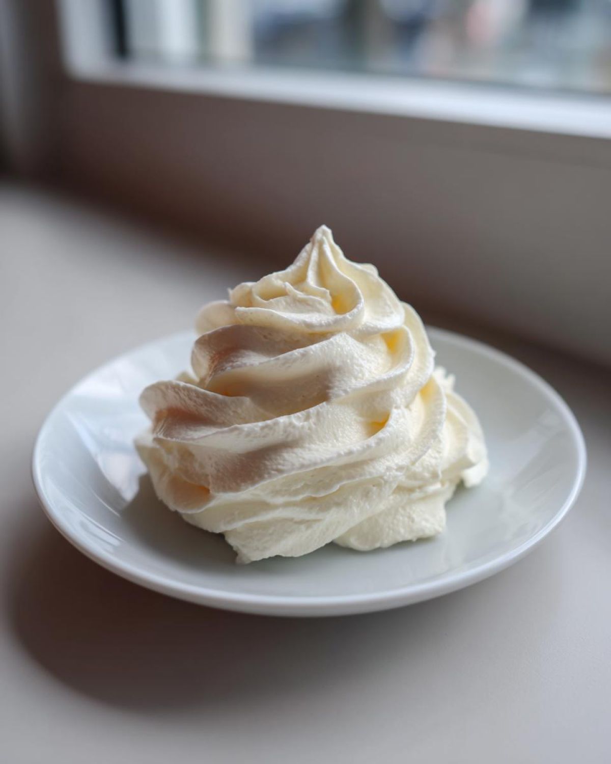 A perfect swirl of thick, white cream cheese frosting piped onto a small white saucer.
